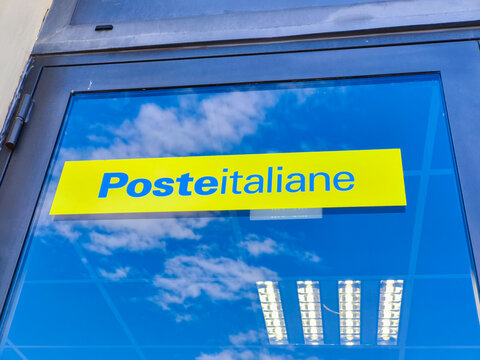 Taormina, Italy - February 07, 2026: Poste Italiane logo displayed prominently on a glass storefront with reflections of clouds and fluorescent lights visible in the window