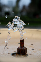 Water Splash from Drinking Fountain in Park &ndash; Blurred Background. Fresh Water Droplets from Resort Drinking Fountain, Shallow Depth of Field