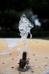 Water Splash from Drinking Fountain in Park &ndash; Blurred Background. Fresh Water Droplets from Resort Drinking Fountain, Shallow Depth of Field