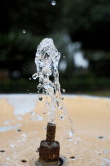 Water Splash from Drinking Fountain in Park &ndash; Blurred Background. Fresh Water Droplets from Resort Drinking Fountain, Shallow Depth of Field