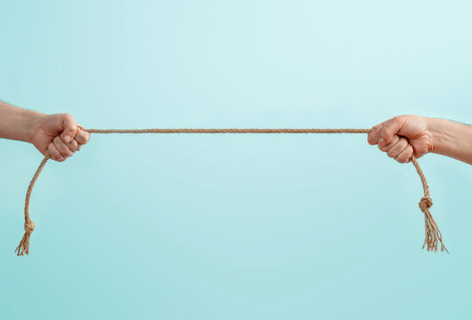 Two people pulling a rope in opposite directions, concept of conflict, power struggle, tension and confrontation, teamwork breakdown and competition