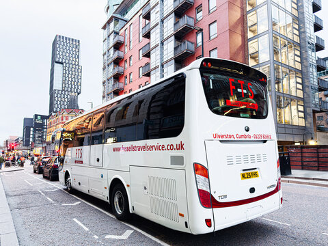 Bus Fussell's Travel Service tour through Manchester city streets with a white coach and modern buildings