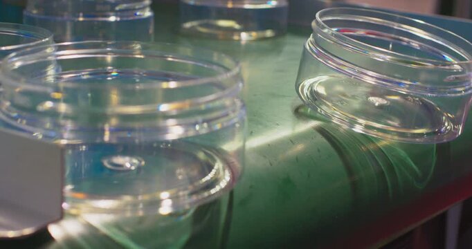 Transparent plastic jars tumble off a green conveyor belt in an industrial plant, showing a production line mishap or recycling process with automation and packaging equipment