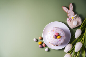 Easter spring cake with chocolate mini eggs, wooden bunny and white tulip flowers. Green background. Top view with copy space