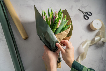 Mother's day, birthday bouquet. Female hands wrapping tulip flowers in craft paper. Spring tulips flower background