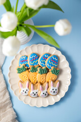 Easter spring holiday background with easter cookies in a plate: bunny, carrot and egg with white tulips in a vase