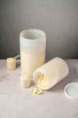 Protein powder in scoops with white plastic protein tubes, jars in background. Body building, muscle growth and food supplement concept