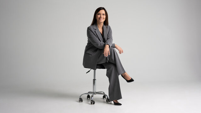 Portrait of a cheerful young businesswoman sitting in a chair against white background.