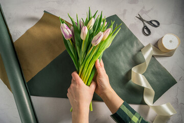 Mother's day, birthday bouquet. Female hands wrapping tulip flowers in craft paper. Spring tulips flower background