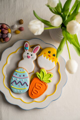 Easter festive colourful cookies bunny, carrot, egg, chick in a plate with egg candies and bouquet of spring tulips