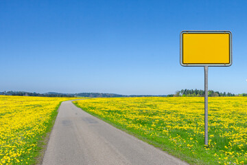 Landstrasse durch eine Landschaft im Fr&uuml;hling mit Ortsschild