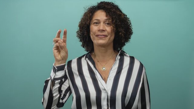 Woman in a striped shirt holds up index finger adorned with a silver ring in a teal studio set; clarity insight confidence focus.
