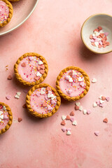 Valentine's day pink background. Pink mini tarts with heart shaped sprinkles. Top view, copy space