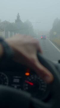 Driver cautiously proceeding on fogcovered village road with emergency signals, Subdued color scene of cautious driving through fog enshrouded village street with flashing emergency lights
