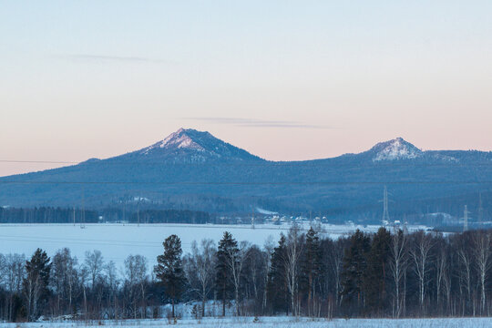 Ural Mountains near the city of Beloretsk, Republic of Bashkortostan. Snow-covered landscape with distant mountains under pastel sky at dawn, serene winter scene in rural area