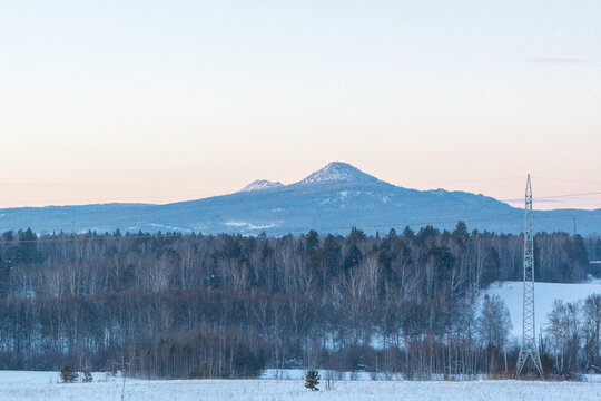 Ural Mountains near the city of Beloretsk, Republic of Bashkortostan. Snow-covered landscape with distant mountains under pastel sky at dawn, serene winter scene in rural area