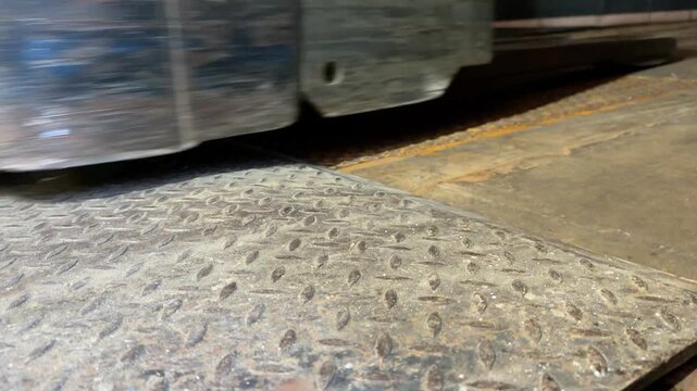 A low angle close up shot of a metal diamond plate dock leveler as an electric pallet jack drives across it into a semi trailer