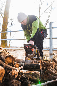 Man cutting wood with chainsaw outdoors in winter