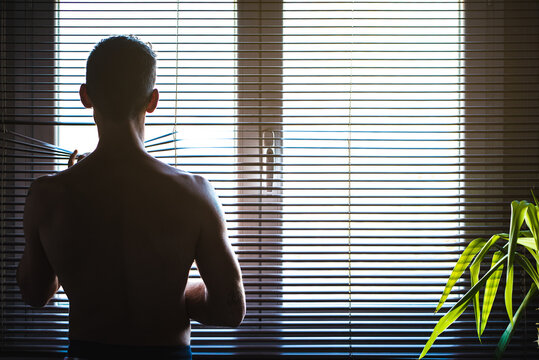 Man looking out window through blinds in sunlight
