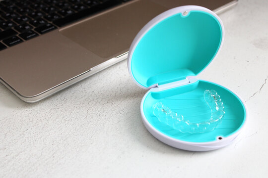 Top side view of a laptop on a desk with an open case containing a transparent dental aligner.
