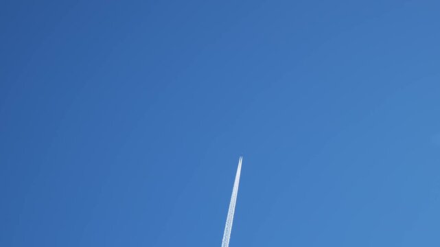 Jet aircraft flying at high altitude leaving long white contrail across clear blue sky. Vapor trail forming and stretching behind airplane during commercial flight. Aviation transport moving through