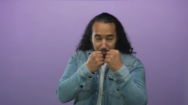 Man with fists raised in boxing guard wearing denim jacket in studio against purple backdrop; strength determination.