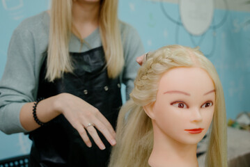 Naklejka premium A hairdressing student practices braiding hair on a mannequin