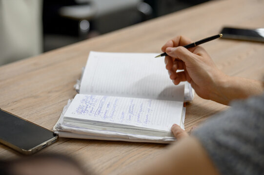 Close-up of a woman's hand with a pen taking notes in a paper notebook