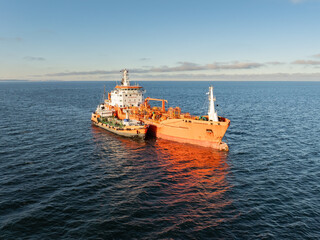 Fototapeta premium Aerial drone view of a large industrial tanker ship receiving fuel from a bunkering vessel in the Baltic Sea waters.