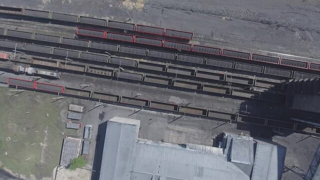 Aerial Drone Footage of Busy Coal Train Yard Freight Trains with Loaded Black Coal in Open Hopper Cars, Industrial Buildings, Multiple Tracks, Operational Activities in Rugged Logistics Facility