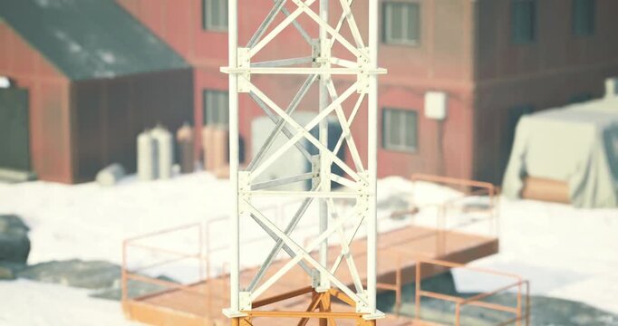 A construction tower stands prominently at an industrial site covered in snow. The winter sunlight illuminates the structure, highlighting its bold colors against the backdrop of buildings.