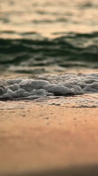 Soft sea waves with white foam washing over a sandy beach during golden sunset with beautiful orange reflections on the water surface in a peaceful tropical landscape with low angle view