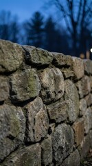 Ancient weathered stone wall with moss-covered rocks stacked in traditional masonry construction against blurred winter landscape background.