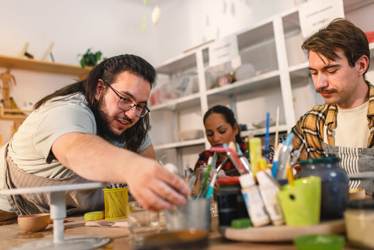 Diverse group of friends attending pottery class havng fun making clay objects together.