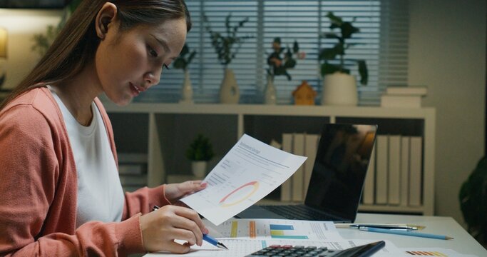 Late night financial planning scene: An Asian woman analyzing investment data, retirement information, and earning potential to ensure future wealth and a stable economy.