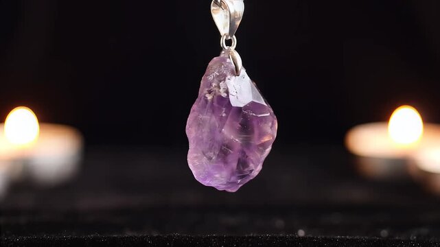 Amethyst crystal pendant hanging against dark background with candle bokeh for jewelry display