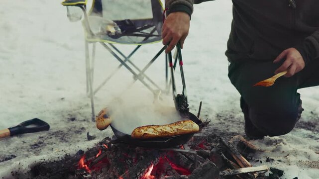 Hiker cooking baguette bread on campfire in winter snow