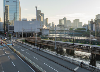 夕日に照らされる川沿いの鉄道とビル群