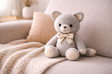 A crocheted teddy bear sits on a couch with a blanket and pillow