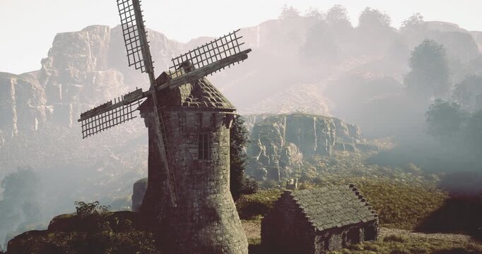 Set against a backdrop of rugged hills, a historic windmill features wooden sails and weathered stone. Nearby, a quaint cottage adds charm to the serene landscape during early morning light.