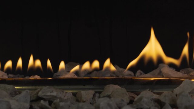 Detailed close-up of a row of vibrant yellow flames emerging from a gas burner tube, surrounded by white decorative pebbles