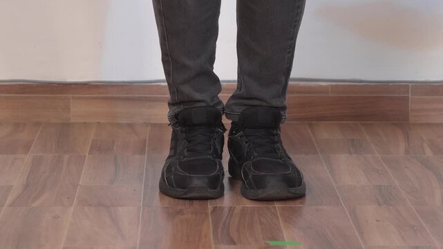 Cropped view of a person wearing black leather dance shoes and gray pants on an indoor floor, making a flamenco dance steps on a wooden platform.