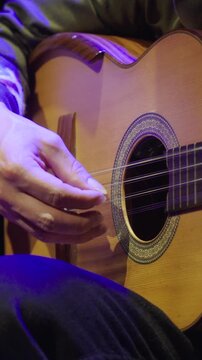 Vertical close-up focusing on a musician's right hand as they play a stringed instrument Tiple. The image emphasizes the long, groomed fingernails used for fingerstyle technique.