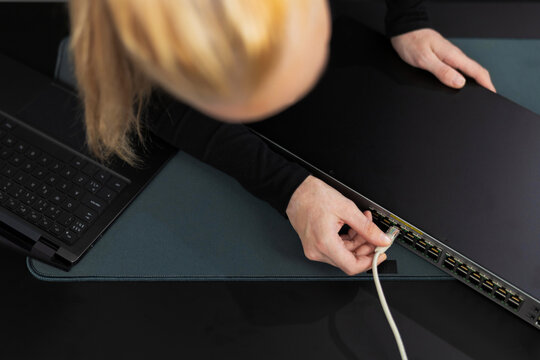 Woman in her 30s with blond hair installs Ethernet cable to network switch in a modern office setting