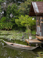 Obraz premium Wooden Rowboat by Rustic Riverside Hut in Lotus Pond.