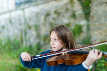 Young girl playing the violin outdoors with a focused expression on her face © august.columbo