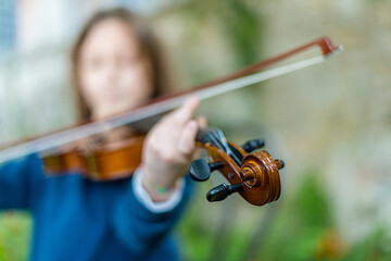 Young girl playing the violin outdoors with a blurred background, focus on the instrument © august.columbo