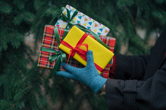 Hand with winter glove holding wrapped gifts outdoors during holiday