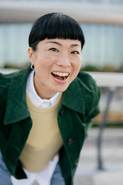 Smiling woman in green jacket outdoors looking at camera in urban setting