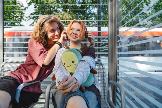 Teenagers sharing headphones and plush toy at urban subway stop